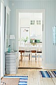 Wood-clad foyer in pastel blue with simple chest of drawers next to open doorway with view into rustic dining room