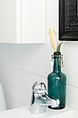 Flower in vintage, swing-top bottle next to tap fitting