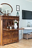 Antique writing desk with vase of flowers on desk panel next to white console table below flatscreen TV on wall in rustic interior