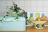 Potted ivy on pastel blue bread bin next to tray with pineapple motif and retro china pot