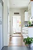 Zeitgenössische Küchenzeile mit weissen Oberflächen; Blick durch offene Tür ins Kinderzimmer