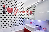 Writing, heart and lipstick on bathroom wall with black polka-dots and mirrored wall with row of spotlight above sink