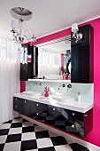 Black washstand with twin sinks below black, wall-mounted cabinet and mirror on hot-pink wall