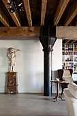 Loft apartment with wood-beamed ceiling, metal pillar, sculpture on plinth, side table and reading chair