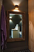 Designer-Waschtisch in Goldrahmenspiegel, violettes Badehandtuch und Holzschrank in stimmungsvoller Beleuchtung