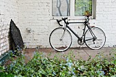Bicycle leaning against whitewashed brick wall behind flowerbed