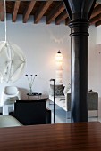 Lounge furniture and standard lamp in renovated loft apartment with black, industrial pillar and rustic, wood-beamed ceiling