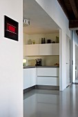 Blick in Nische mit eingebauter weißer Küche Übereck und glänzendem grauem Kunstharzboden