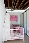 Pink-painted twin cots with white canopies and fitted wardrobes below rustic wood-beamed ceiling