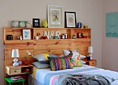 Double bed with colourful scatter cushions and wooden headboard panel with youthful ornaments on integrated shelves and bedside table