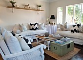 Vintage-style living room with scatter cushions on white sofas, wicker armchair, coffee table and stacked magazines on wooden trunk