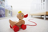 Wooden pull-along duck next to cot on white carpet