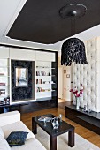 Elegantes Wohnzimmer mit postmodernen Elementen; Hängelampe mit Schlaufenschirm, im Hintergrund ein Einbauregal mit Spiegelnische
