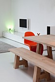 Wooden dining table and matching bench; spotlight on low, white sideboard in background