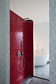 Shower area with red mosaic tiles; view of bathtub through open doorway