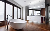 Modern, free-standing bathtub with floor-mounted tap fittings on walnut parquet floor in designer bathroom with floor-to-ceiling, frosted windows