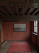 Rug on wooden floor and picture on rusty red wall in minimalist, rusty interior