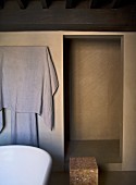 Edge of bathtub, towel on wall-mounted rack and shower area in minimalist bathroom