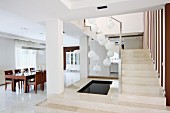Pale stone staircase and platform with sunken pool below spherical pendant lamps and dining area to one side in elegant interior