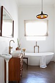Purist tap fittings, designer bathtub, washstand with drawers, mirror, scales and retro-style light fitting in bathroom