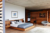 Wood-framed double bed with bedside tables integrated in headboard, grey easy chair and wooden partition in modern bedroom