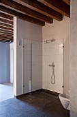 Minimalist, easy-access shower with glass screens in loft apartment with wood-beamed ceiling