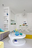 Colourful glass containers on round, white coffee table; white fitted kitchen with dining table in background