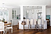 Upholstered bar stool at counter with white wooden frame below glass pendant lamps in open-plan kitchen