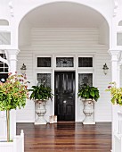Veranda with white-painted archway and wooden floor leading to elegant front door flanked by antique planters