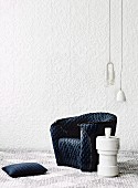 Armchair with quilted, charcoal-grey loose cover, pendant lamps and plinth-style side table against white structured wallpaper