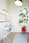Simple bathroom with white and blue striped rug, trolley below window and trough-style sink to one side