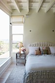 Bed with upholstered headboard and ruffled bedspread in bedroom with white wooden ceiling