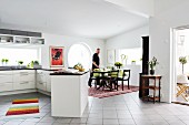 White, open-plan kitchen with expansive counter and man in traditional-style dining area to one side in open-plan interior