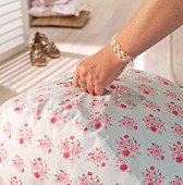Pouffe with handle and hand-sewn, floral cover held by woman's hand with jewellery
