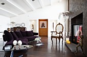 Modernes, violettes Sofa und Rokoko Stuhl vor offenem künstlerisch gestaltetem Kamin in offenem Loft-Wohnraum mit weiß gestrichener Rippendecke
