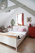 Rustic sleigh bed with white wooden frame in simple attic room with exposed wooden roof structure