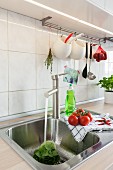 A stainless steel sink with kitchen utensils hanging above it on a pole in a renovated kitchen
