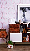 Alphabet bookends on fifties-style sideboard with open-fronted sections and cabinet doors below framed photo on patterned wallpaper