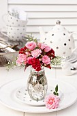 Bouquet of roses with cockscomb and gypsophila in silvered glass vase in front of polka-dot tea set