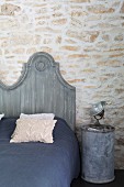 Grey-painted bed headboard next to spotlight on metal can used as bedside table against stone wall