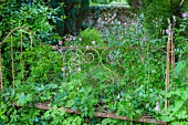 Ornate, metal bed frame overgrown with plants in summery garden