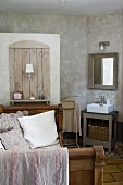 Antique bed with high foot and headboard, shelf and lamp against wall element screening toilet next to simple washstand