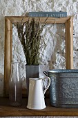 Stillleben mit Vintage Gefässen aus Zink, Emaille und Glas, Lavendel Trockenstrauss und Holzrahmen vor grob verputzter Wand