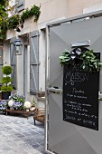 Open courtyard gate with shop opening times on hand-written chalk board and view into charming, rustic courtyard