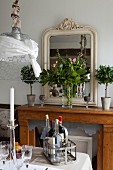 Antique mirror and vase of peonies on console table; bottles of wine in vintage bottle carriers on set table