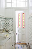 Twin washstand in narrow bathroom with traditional tiles and stained glass elements in panelled door