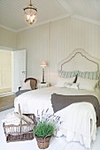Basket and potted lavender at foot of double bed with elegant headboard