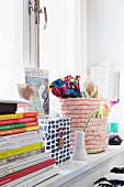Stacked books, decorative storage box and woven basket on windowsill