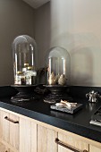 Collectors' items under glass covers on kitchen counter with black worksurface