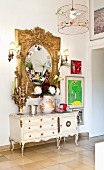 White Rococo-style cabinet below ornate gilt-framed mirror combined with modern artworks and photos in hallway